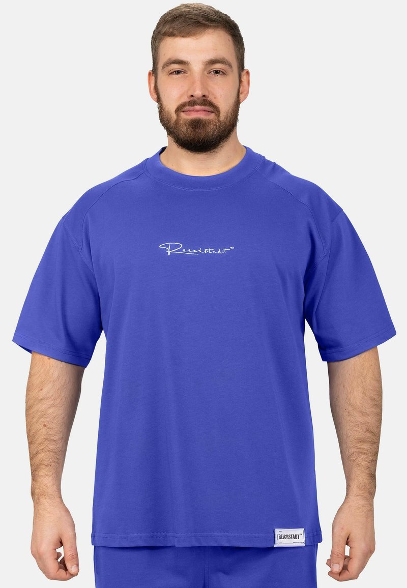 T-shirt à manches courtes en bleu vif, fabriqué en coton doux. Il présente un logo blanc sur la poitrine et un ourlet droit avec une étiquette sur le côté.