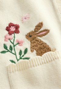 Tikandiga kujundus, millel on pruun jänes roosa ja punase lille kõrval kreemja kangapõhja peal, alumises servas soonikkand.