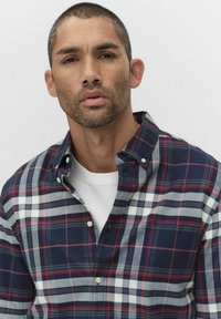 Koszula flanelowa w granatową, czerwoną i białą kratę. Posiada kołnierzyk zapinany na guziki oraz kieszeń na piersi. Nosi się na białym t-shircie z okrągłym dekoltem.