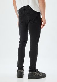 Jeans de mezclilla negros con un corte ajustado, que cuentan con bolsillos traseros y una cinturilla de altura media, acompañados de unas zapatillas negras texturizadas.