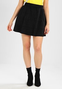 Svart kordskjol med ett flerfaldigt mönster, försedd med elastisk midja. Tyget har en mjuk textur, tillsammans med åtsittande svarta stövlar.