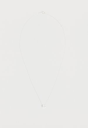 Collier délicat en chaîne d'argent avec un petit pendentif circulaire présentant une découpe en croissant de lune, exposé sur un fond clair uni.