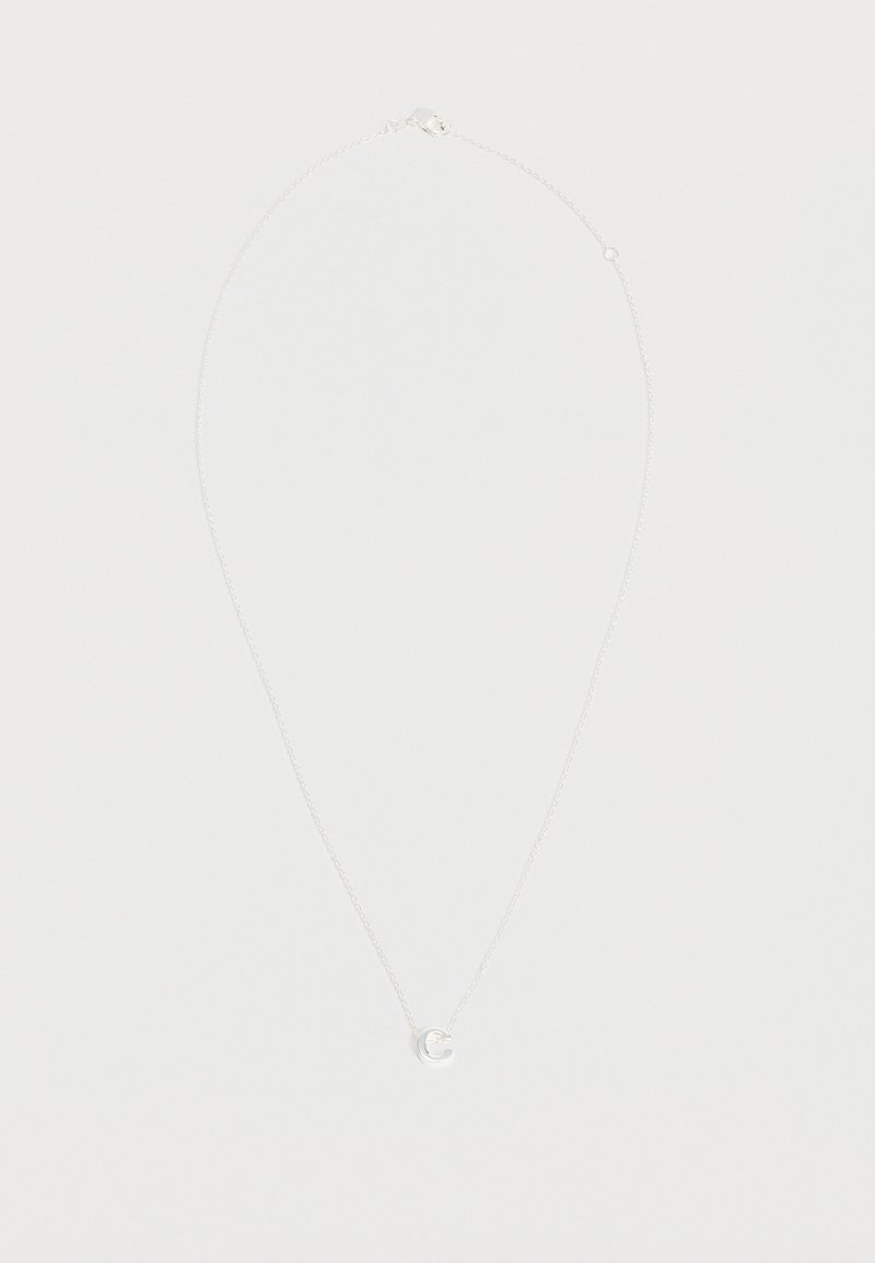 Collier délicat en chaîne d'argent avec un petit pendentif circulaire présentant une découpe en croissant de lune, exposé sur un fond clair uni.
