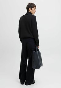 Suéter negro de cuello alto acanalado, pantalones oscuros de pierna ancha, sosteniendo un bolso tote estructurado negro. Diseño minimalista, tejido texturizado, líneas limpias.