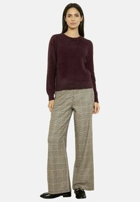 Maglione borgogna peloso con colletto rotondo, abbinato a pantaloni a gamba larga con motivo tartan beige e marrone scuro, completato da scarpe nere.