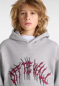 Sudadera gris con capucha que presenta un diseño de texto bordado en negro y rojo con un estilo irregular en la parte frontal. Tela suave, corte casual.