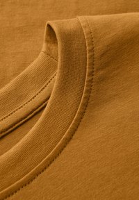 Hnědý bavlněný tričko s límečkem, hladká textura, žebrovaný okraj, čisté švy, s jemným leskem, který zdůrazňuje měkkost tkaniny.