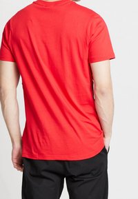 Camiseta de algodón roja con un clásico cuello redondo y mangas cortas, que presenta una textura suave y una silueta ajustada.