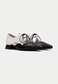 Chaussures en cuir noir et blanc avec un bout pointu, un petit talon carré et un délicat détail de laçage sur le panneau blanc. Texture lisse sur l'ensemble.