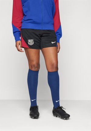 Pantaloni sportivi neri con logo del Barcellona, abbinati a calze blu fino al ginocchio e scarpe nere con il simbolo bianco di Nike.