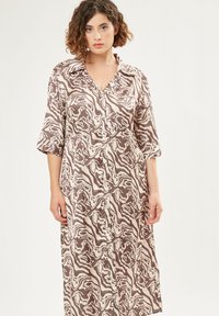 Kleid mit Knopfleiste aus seidig-glattem Stoff, das ein braun-creamfarbenes abstraktes Muster aufweist, mit einem Kragen und drei Viertel Ärmeln.