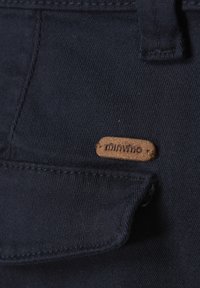 Donker marineblauwe stof met een zachte textuur, voorzien van een voorzak en een bruin leren label met de tekst "minymo" er op gestikt.