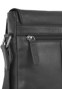 Schwarze Leder-Umhängetasche mit einem Reißverschlussfach, verstärkten Nähten und verstellbarem Tragegurt. Subtile Textur mit glatter Oberfläche.
