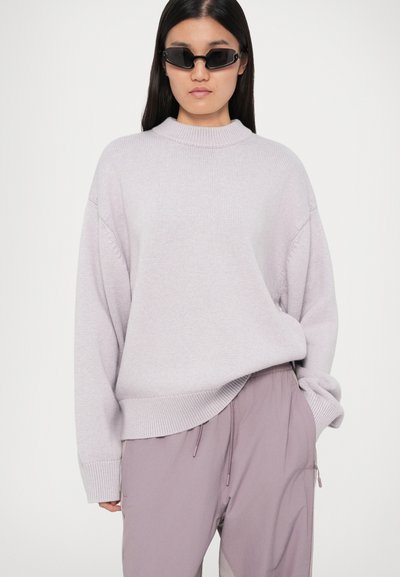 Suéter de lavanda claro com gola alta, bainha canelada e ombros caídos, combinado com calças largas de púrpura claro com fechos laterais.