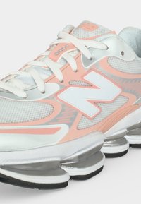 Λευκό και ροδακινί αθλητικό παπούτσι New Balance με ύφασμα από δίχτυ, κλείσιμο με κορδόνια, μεγάλο λογότυπο "N" και τμηματική ασημένια σόλα για απορρόφηση κραδασμών.