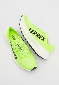 Lime zöld futócipők fekete "TERREX" felirattal, hálós felsőrész, párnázott nyak és vastag fehér középtalppal, valamint bordázott fekete külső talppal.