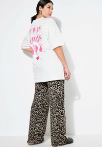 T-shirt bianco oversize con testo rosa sul retro. Un paio di pantaloni larghi con design a stampa leopardata marrone e nera.