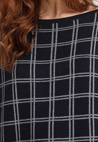 Maglione blu navy con un motivo a griglia grigia, caratterizzato da un ampio scollo e tessuto testurizzato, che presenta una vestibilità rilassata e un design morbido.