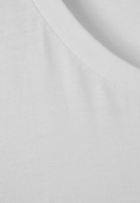 Hvidt bomuldsstof i nærbillede, der viser tekstur og syninger på et foldet område med rund hals.