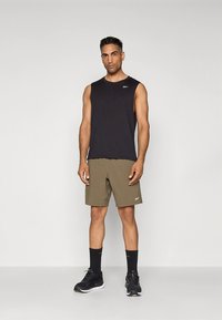 Juoda rankovių palaidinė ir alyvuogių žaliumo šortai, derinami su juodais sportbačiais ir atitinkančiomis kojinėmis. Paprastas dizainas be raštų ar akcentų.