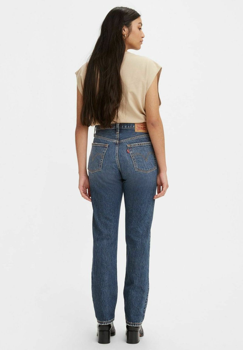 Vaqueros de denim azul de cintura alta con pierna recta, que cuentan con dos bolsillos traseros y un parche de cuero con marca en la cinturilla.