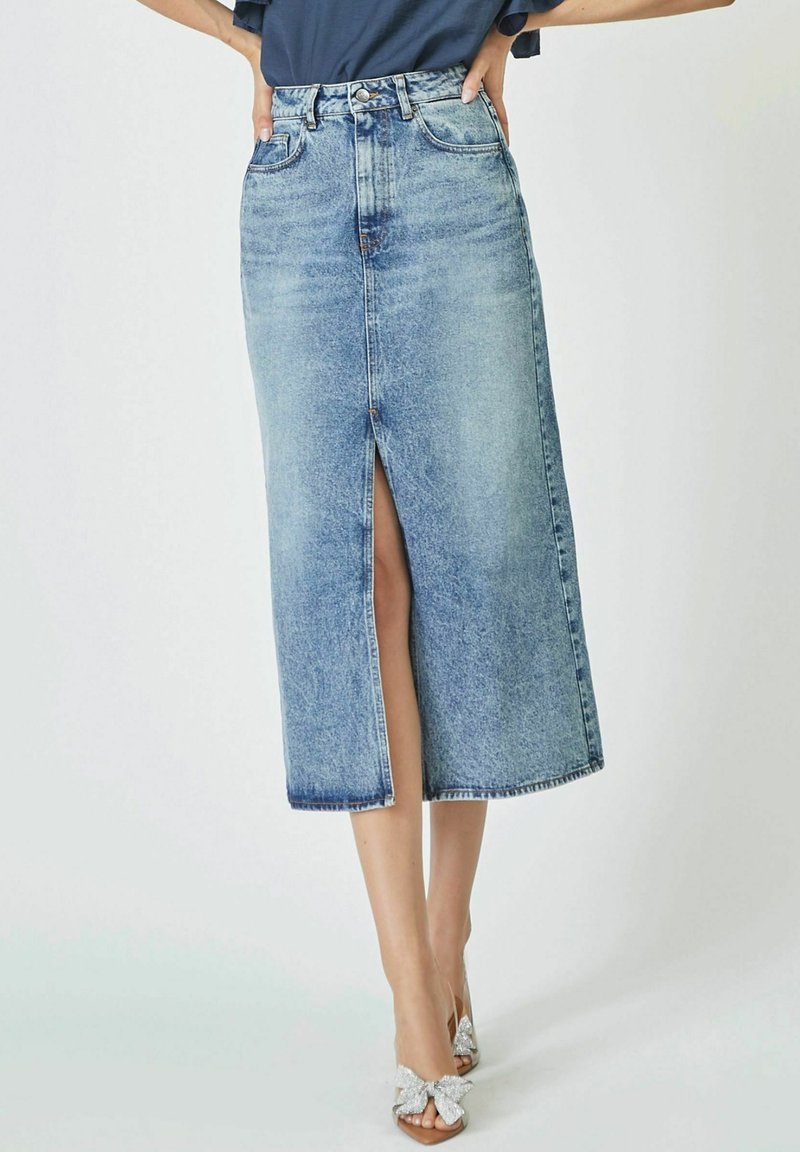 Svetlo modra denim midi krila z sprednjim razporkom, visokim pasom in surovim robom. V kombinaciji s sandali s srebrnimi detalji v obliki pentlje.