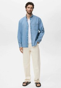 Ljusblå denimskjorta med knappstängning, en bröstficka; i kombination med krämfärgade byxor och svarta sandaler. Minimalistisk design.