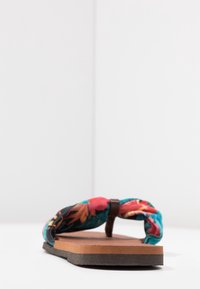 Infradito colorata con fantasia floreale e cinturino intrecciato in tessuto, con soletta marrone e suola in gomma scura.