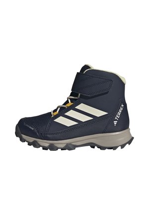 Navyblauwe hoge wandelschoen met witte Adidas strepen, klittenbandsluiting, robuuste zool en "TERREX" logo aan de hielzijde.