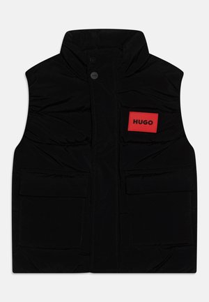 Gilet matelassé noir avec col montant, fermeture à boutons sur le devant, et deux grandes poches avant. Présente un patch rectangulaire rouge avec l'étiquette "HUGO".
