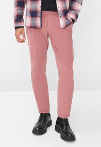 Pantaloni in corduroy color rosa dusty, con vestibilità slim, texture a righe verticali e vita regolabile con cordino, abbinati a scarpe nere.