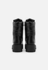 Botas negras hasta el tobillo con un diseño acolchado, textura brillante y una suela de goma gruesa y estriada. Presentan un cierre de cremallera y detalles de costura vertical.