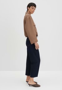 Bruine cropped jacket met een kraag, een voorzak, gecombineerd met donkerblauwe wijde jeans en bruine instapschoenen. Glad, gestructureerd materiaal.