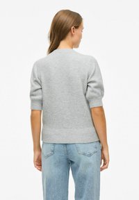 Grijze gebreide trui met korte mouwen en ribbelzoom, gecombineerd met lichtblauwe high-waisted jeans, gezien vanuit de achterkant.
