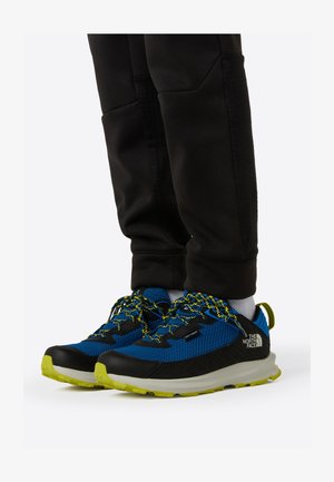 Blå og svarte tursko med teksturert mesh-overdel, grønne detaljer og mønstrede lisser, med en robust såle for godt grep.