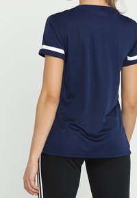 Marinblå t-shirt med kort ärm i atletisk stil, prydd med vita randiga detaljer på ärmarna, tillverkad av ett mjukt och lätt material.