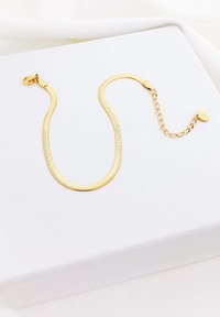 Pulsera de eslabones dorados con un diseño plano y suave, que cuenta con un cierre y una cadena ajustable con un charm circular al final.