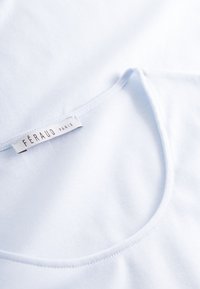 Hellblauer Baumwollstoff mit rundem Ausschnitt und weicher Textur. Enthält ein sichtbares Etikett mit der Aufschrift "FÉRAUD PARIS" am Rand.