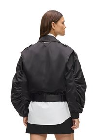 Giacca in raso nero con maniche a sbuffo, vita con cintura e scollo con colletto. Presenta una texture liscia e un design minimalista.