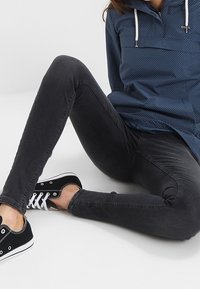 Ciemnoszare skinny jeans w połączeniu z niebieskim pulowerem w kropki, z pół-zamkiem i kapturem. Czarne sneakersy z białymi akcentami dopełniają całość.