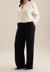 Bílé dlouhé rukávy s košilovým límečkem, kombinované s námořnickými širokými kalhotami a černými sandály s otevřenou špičkou. Hladká textura.