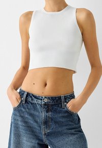 Top corto bianco a righe con scollatura tonda, abbinato a jeans in denim blu a vita alta con chiusura a bottone e tasche frontali.