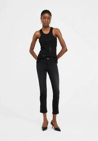 Juoda bakas su subtiliais papuošimais, derinamas su aptemptomis juodomis džinsomis, kurios šiek tiek trumpesnės ir turi šonines sagų detales. Juodi aukštakulniai.