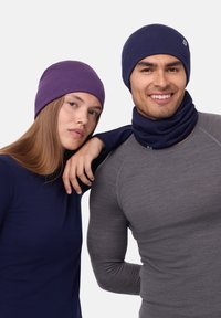Two individuals wear winter accessories: a purple beanie and a navy beanie, along with a navy neck gaiter and a gray long-sleeve shirt.