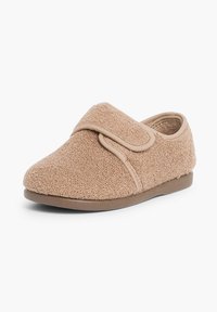 Zapatilla de tela color canela con una superficie texturizada, correa de velcro en el empeine, punta redondeada y suela blanda y plana.