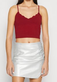Top corto burdeos con escote con volantes y tirantes finos; combinado con una minifalda plateada, brillante, con fruncidos y un dobladillo diagonal.