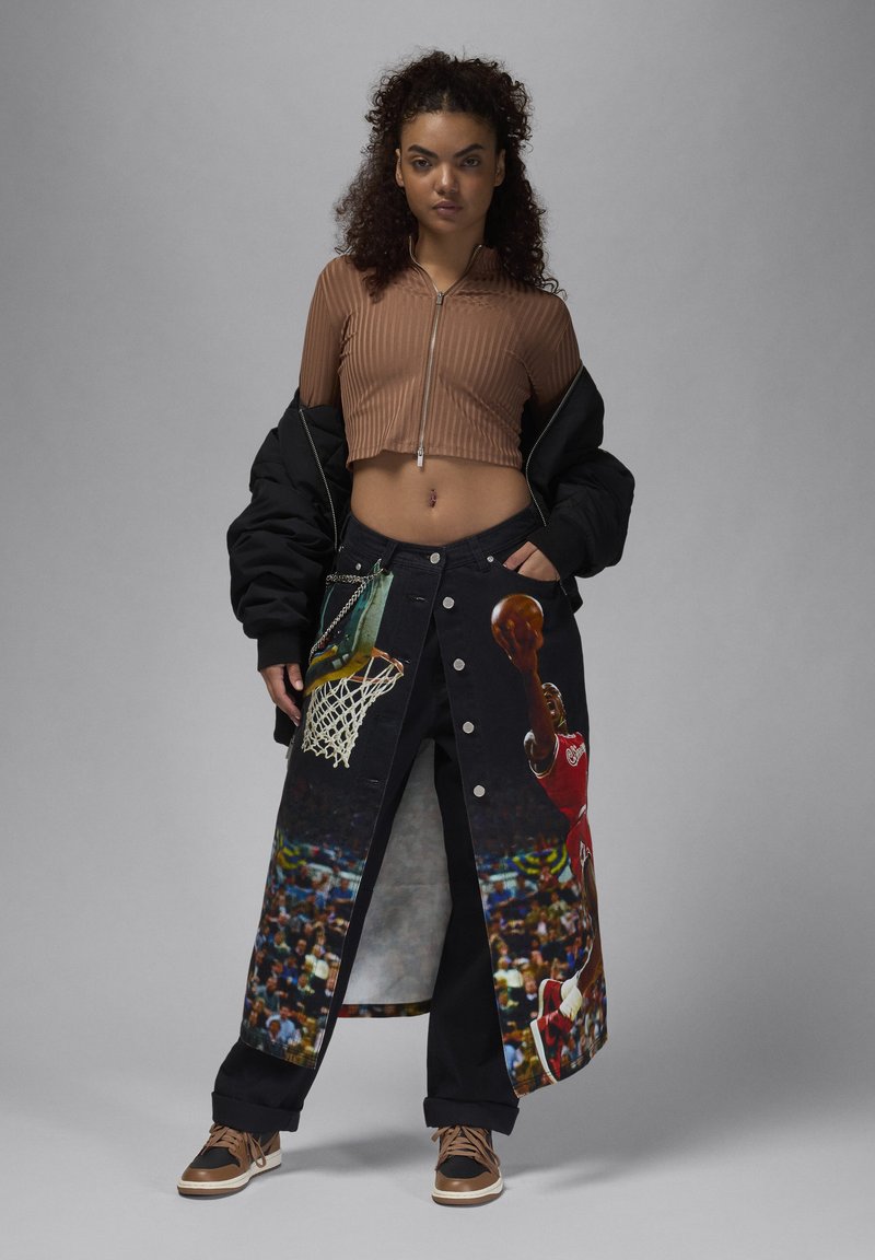 Falda de mezclilla con estampados gráficos de temática deportiva, tejido negro, cierre de botón, combinada con un crop top de canalé marrón y una chaqueta de plumas negra.