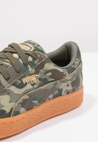 Snikers med kamouflage-mönster i grön och beige, läderöverdel, gummisula och guld-logotyp. Klassisk lågmodell.