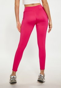 Aansluitende roze leggings met een hoge tailleband, een gladde textuur en een full-length ontwerp, gecombineerd met grijze sportschoenen.