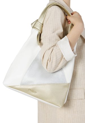 Persona con traje beige sostiene un gran bolso de hombro de cuero blanco y dorado con detalles metálicos texturizados.